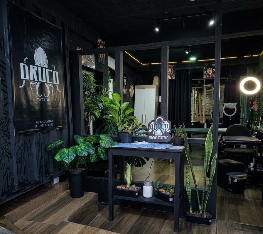 Entrada do estúdio Druco Tattoo com plantas, banner do polvo e vista do interior acolhedor em São Thomé das Letras